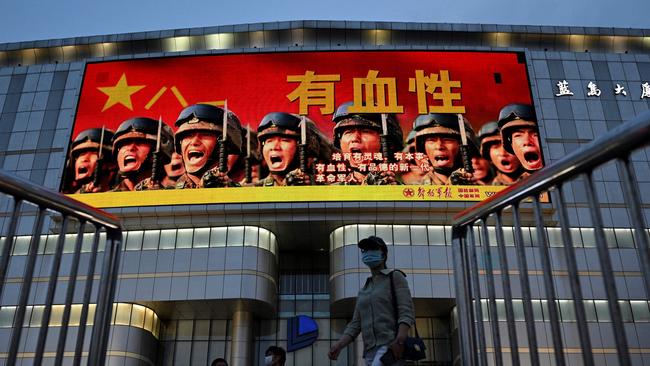 People walk along a Beijing street underneath a Chinese military propaganda signs which reads: “Courageous – raise a new generation of spirited, capable, courageous and morally upright revolutionary soldiers”. Picture: AFP