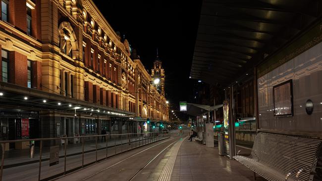 A lone commuter sits at a tram stop outside a deserted Flinders Street Station after curfew.