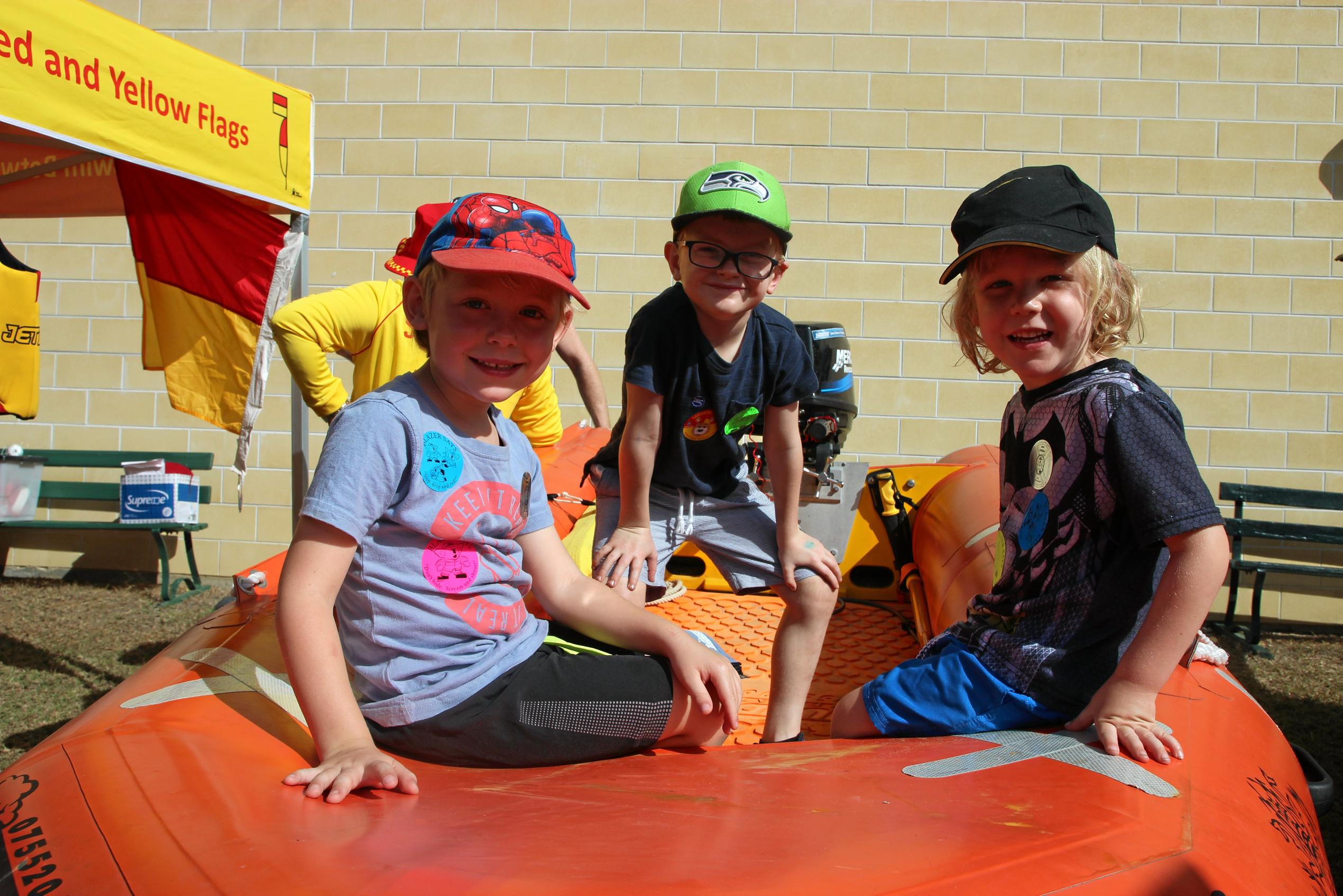 (From left): Henry Brewer, Oliver Krehlik and Otis Brewer hitch a ride in a Surf Lifesaving boat at the Heritage Village on Sunday. Picture: Shayla Bulloch