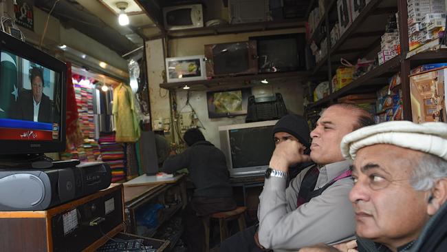 Pakistani shopkeepers watch as Prime Minister Imran Khan addressed the nation. Picture: AFP