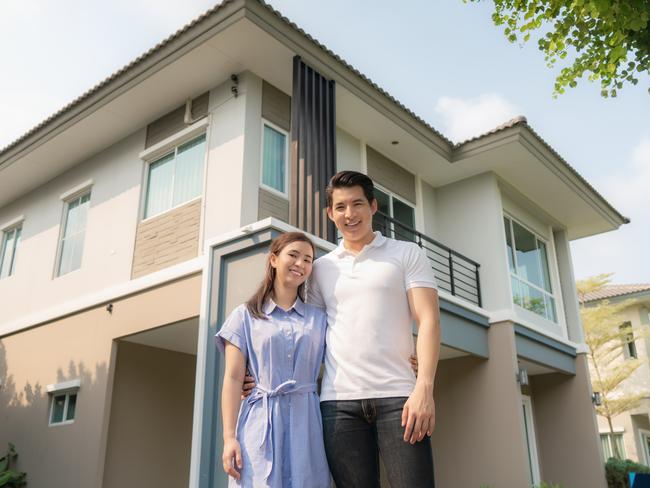 Portrait of young couple standing and hugging together looking happy in front of their new house.  home loan generic