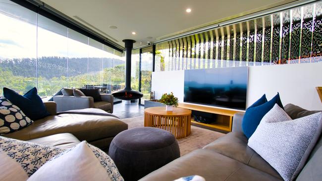 A suspended fireplace features in the open-plan living room where huge windows frame surrounding bushland.