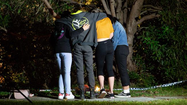 A group of friends pay their respects and lay flowers at the scene.