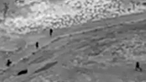 An officer and his police dog (far left shadow) keep an eye on two suspects laying on the ground (long shadow second from left) from the other side of a fence as three other police officers descend on their position. Drone image: NT Police