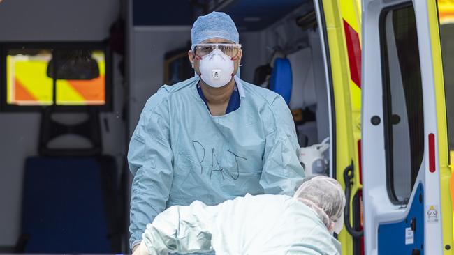 An NHS workers in PPE lifts a patient from an ambulance at St Thomas' Hospital in London.