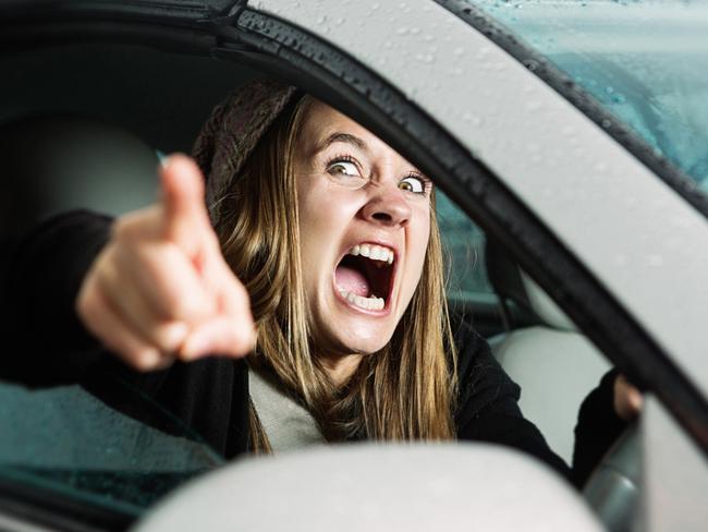 A young woman yells and points at something or someone in a fit of road rage, seen through her car window.