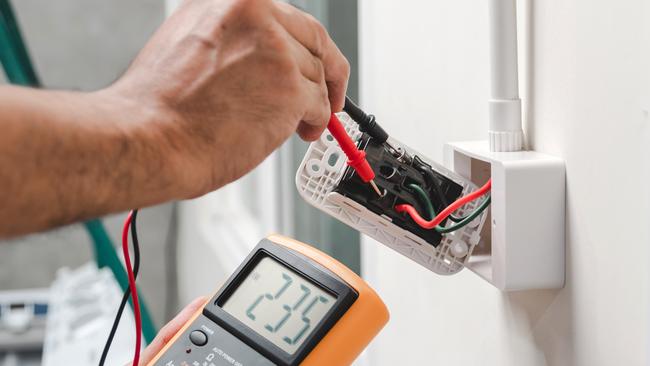 Electrician is using a digital meter to measure the voltage at the power outlet in on the wall.