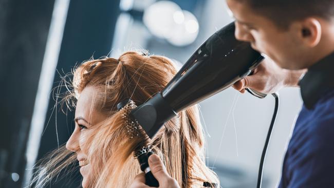 Young hairdresser drying customers hair with round brush at hair salon. Hairdresser generic