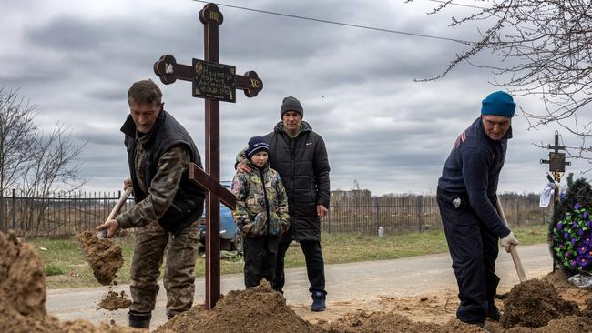 Grave diggers shovel soil into the grave of a woman as her husband and son watch on April 20 in Bucha, Ukraine.