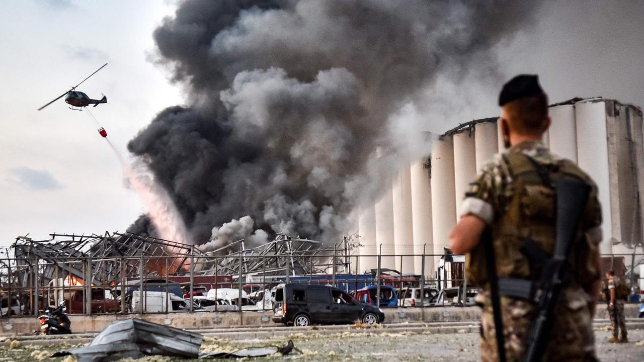 Lebanese army soldiers stand while behind a helicopter puts out the fire. Picture: AFP