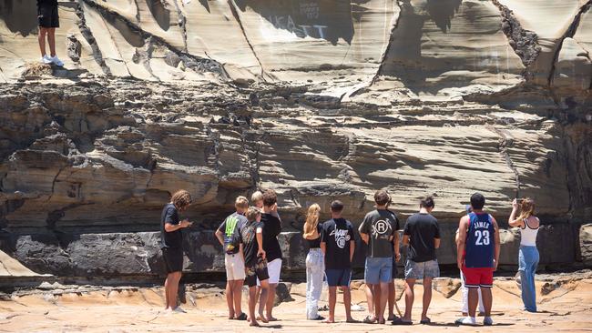 Friends of Luca Bennett scratch his name into the rock at North Avoca where he was swept into the ocean on Christmas Eve. Picture: Tom Parrish