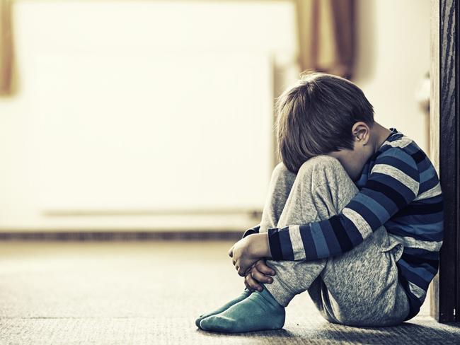 Depressed sad child sitting on the floor, in the door. The little boy is hiding his head between legs.