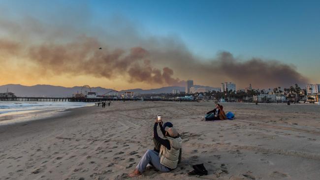 A woman takes a picture on the beach with the Santa Monica pier on the background with smoke from the Palisades Fire seen in the sky. Picture: Getty Images via AFP