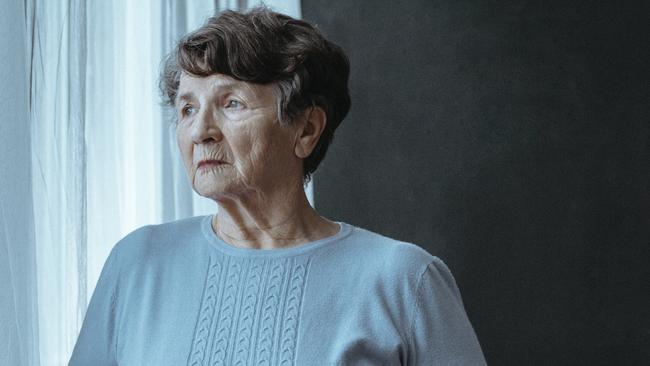 Copy space of blind elderly woman next to window with folded white cane against black background