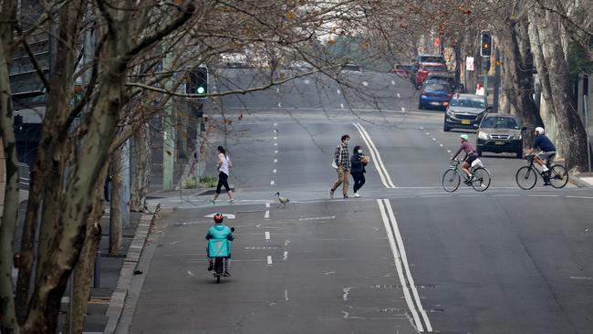 Masked pedestrians, cyclists and delivery riders scattered across a quiet treet in Sydney. Picture: Dylan Coker