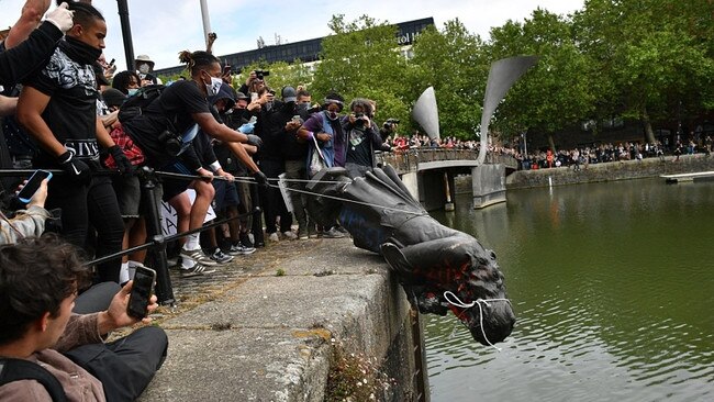 Protesters throwing a statue into a river as part of a “cancel culture” ritual.