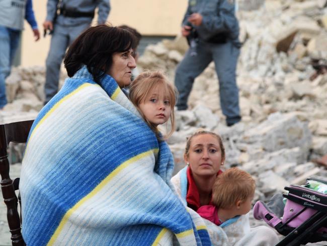 Victims of the quake sit in a huddle as authorities scramble to reach the 69 hamelts affected. Picture: AFP/FILIPPO MONTEFORTE