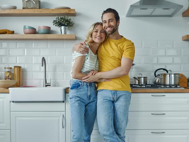 Full length of young couple embracing while standing at the domestic kitchen