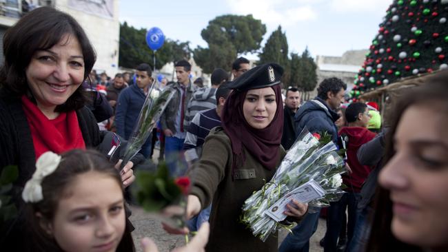 A Palestinian policewoman gives out flowers outside the Church of the Nativity on Christmas Eve in Bethlehem, West Bank. Every Christmas pilgrims travel to the church where a gold star embedded in the floor marks the spot where Jesus was believed to have been born. Picture: Lior Mizrahi/Getty Images