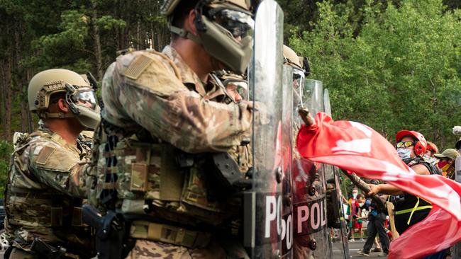 A protester hits the shields of National Guard troops as they block the road to Mount Rushmore National Monument with vans: Picture: AFP