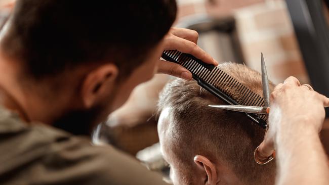 Generic male hairdresser does haircut for bearded man in barber shop.