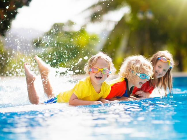 Kids play in swimming pool. Children learn to swim in outdoor pool of tropical resort during family summer vacation. Water and splash fun for young kid on holiday. Sun protection for child and baby.