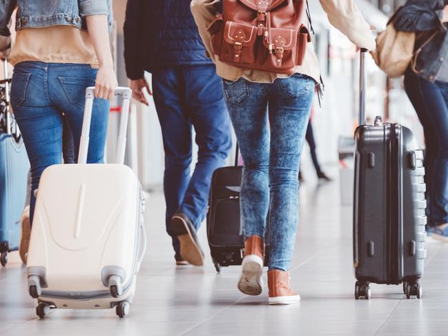 Low angle rear view of passengers walking in the airport terminal. People with luggage in airport.