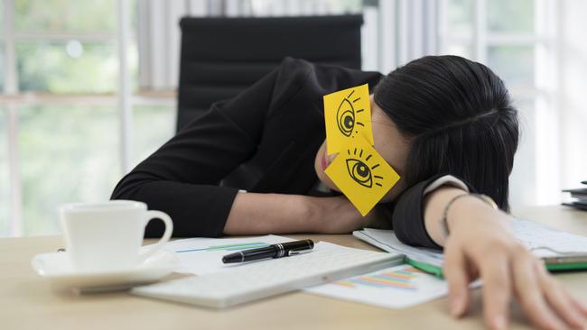 Young business woman with fake eyes painted on adhesive note sleeping at workplace in office