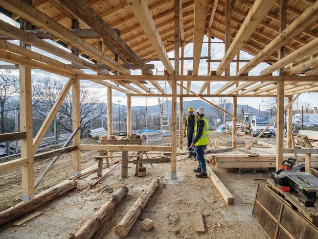 Construction workers in building site of wooden house.