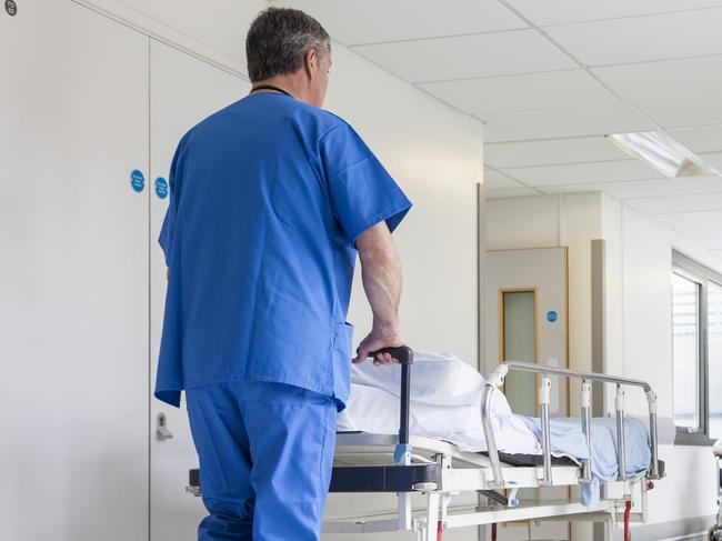 Male nurse pushing stretcher gurney bed in hospital corridor with doctors & senior female patient