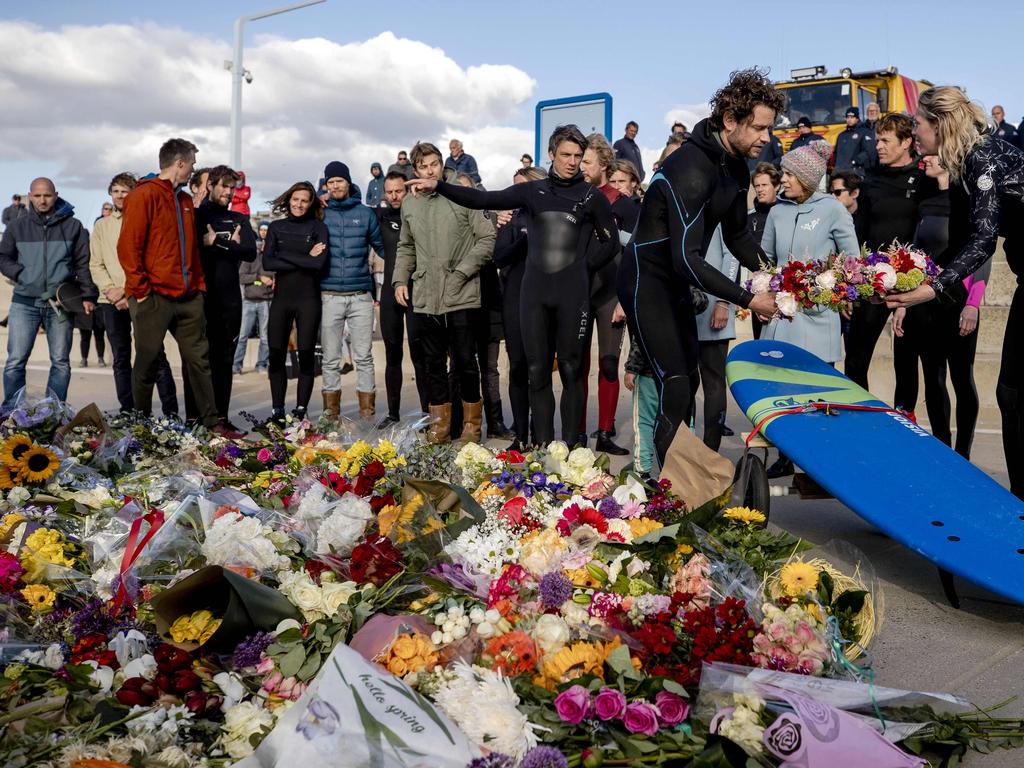 Mourners gather beside floral tributes during a commemoration for the five deceased surfers.