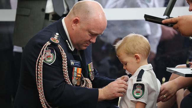 Mr Fitzsimmons pins a posthumous service medal on Harvey Keaton whose dad Geoffrey Keaton died fighting the fires. Picture: James Morris/NSW RFS Media Services