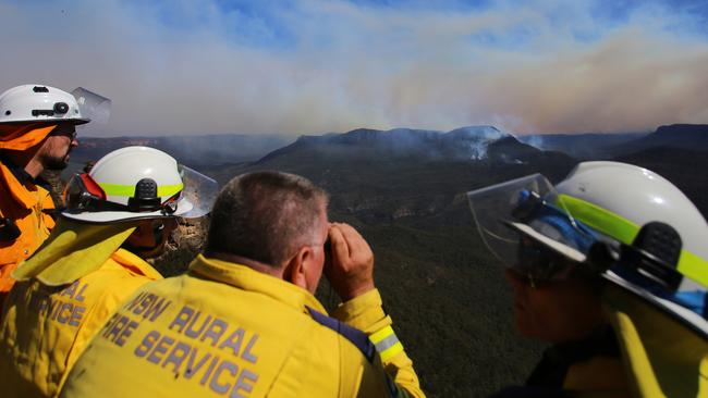 Smoke from the Green Wattle Creek fire is seen in the distance as NSW RFS crew monitor the remnants of the Ruined Castle fire in Jamison valley from Echo Point lookout on December 6. Picture: AAP Image/Steven Saphore