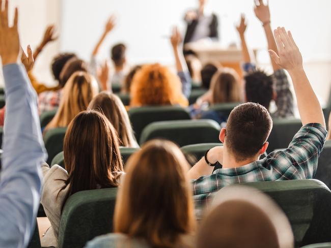 Back view of college students raising their arms on a class at lecture hall.