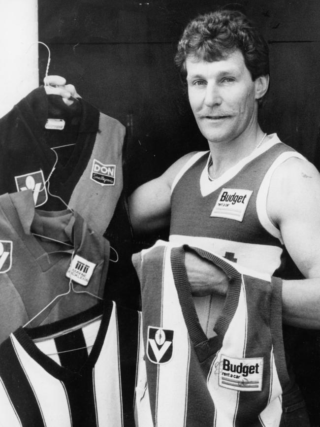 Carman ahead of his 100th game, holding the jumpers of the other clubs he played for.