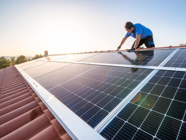 kneeling professional fixing solar panels from the top of a house roof, side view of the roof with sun reflection