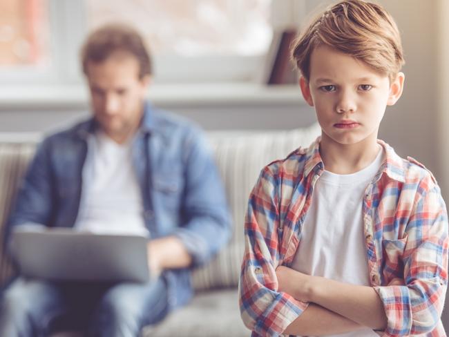 Sad little boy is looking at camera while his father is working in the background