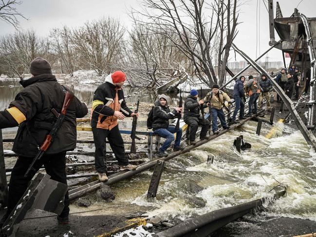 Members of an Ukrainian civil defence unit pass new assault rifles to the opposite side of a blown up bridge on Kyivâ. Picture: AFP