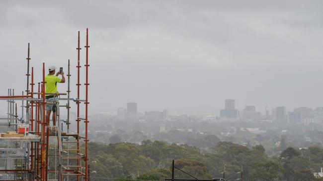 A construction worker at Hamilton Hills snaps haze over the CBD. Picture: AAP/ Brenton Edwards