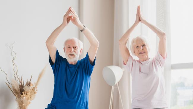 Fit sporty senior old elderly couple family spouses grandparents training stretching doing yoga exercises at home on lockdown together keeping balance on one foot.; active retirement generic