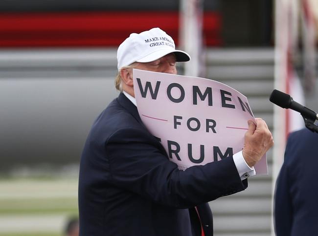 Donald Trump holds a sign that reads 'Women for Trump' during his 2016 presidential campaign, which was beset by scandal over his treatment of women