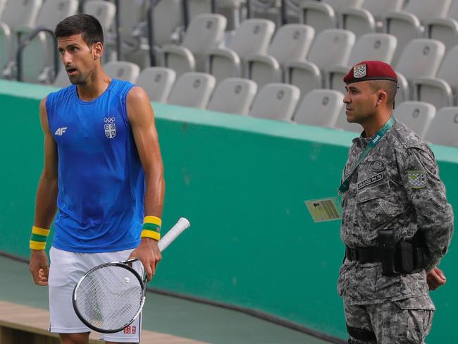 A Brazilian soldier stands guard while Novak Djokovic trains.