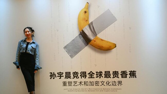 A woman poses for a photo in front of a poster depicting the Comedian a banana artwork bought by Chinese-born crypto founder Justin Sun for $10m. Picture: AFP