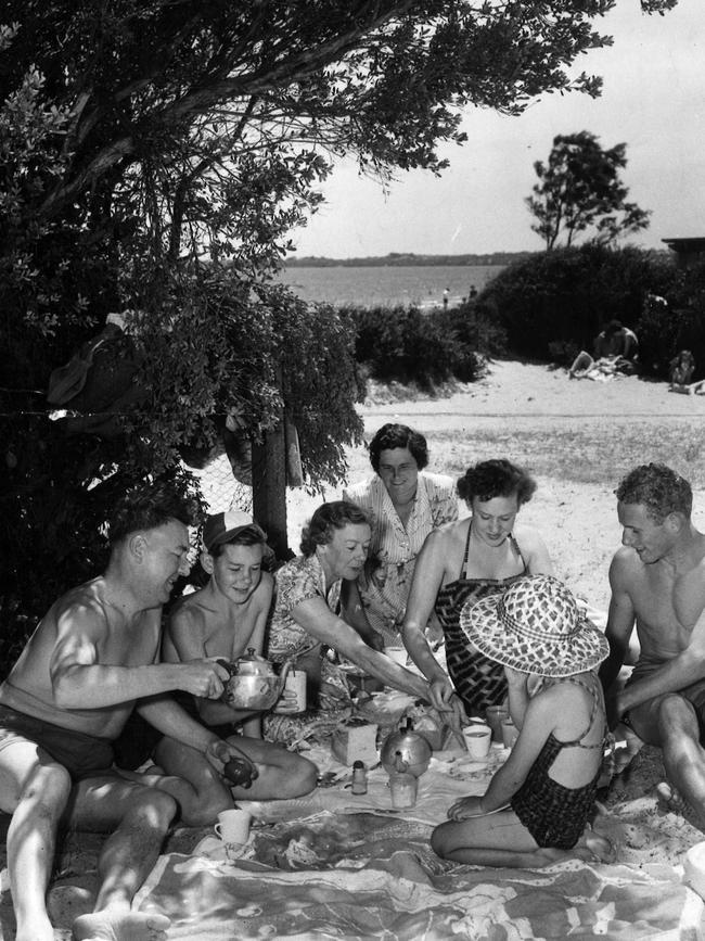 Under the shade of a ti-tree and with the Mordialloc beach in the background, picnic lunches are to be seen everywhere on Boxing Day 1953. Picture: Argus Collection