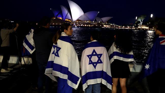 People with Israeli flags watch the Opera House while it is illuminated in blue to show solidarity with Israel in Sydney on October 9, 2023. Israel relentlessly pounded the Gaza Strip overnight and into October 9 as fighting with Hamas continued around the Gaza Strip, as the death toll from the war against the Palestinian militants surged above 1,100. (Photo by David GRAY / AFP)