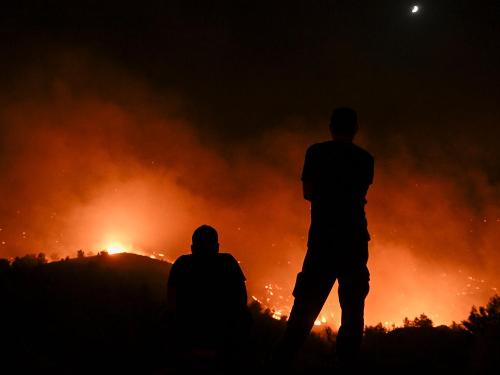 TOPSHOT - People watch the fires near the village of Malona in the Greek island of Rhodes on July 23, 2023. Tens of thousands of people fled wildfires on the Greek island of Rhodes on July 23, 2023, as terrified tourists scrambled to get home. Firefighters tackled blazes that erupted in peak tourism season, sparking the country's largest-ever wildfire evacuation -- and leaving flights and holidays cancelled. (Photo by SPYROS BAKALIS / AFP)