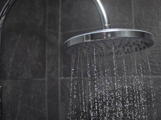 Modern large shower head spraying water, black slate tiled wall behind.Large shower head spraying water - Stock image ipad generic