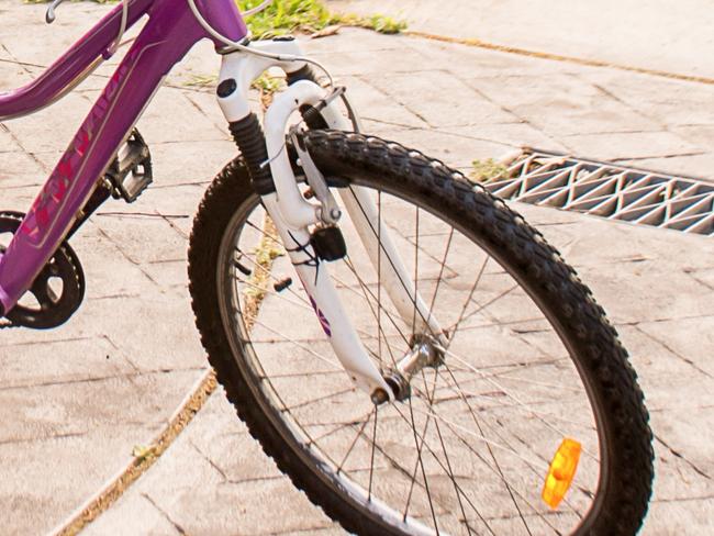 A girl wearing maroon school unfiform and bike helmet going to school on her bicycle. School students return to classrooms after COVID-19 outbreak in Australia