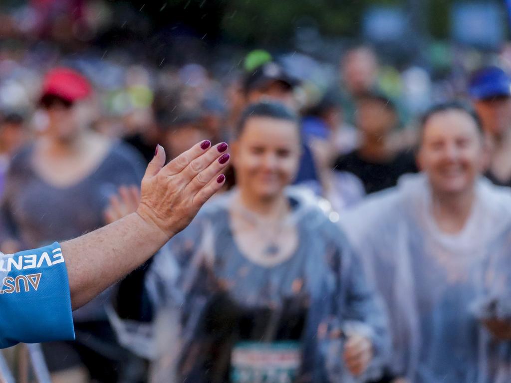 A volunteer high-fives competitors at the start of the very wet Southern Cross University 10 kilometre Run. Picture: Tim Marsden.