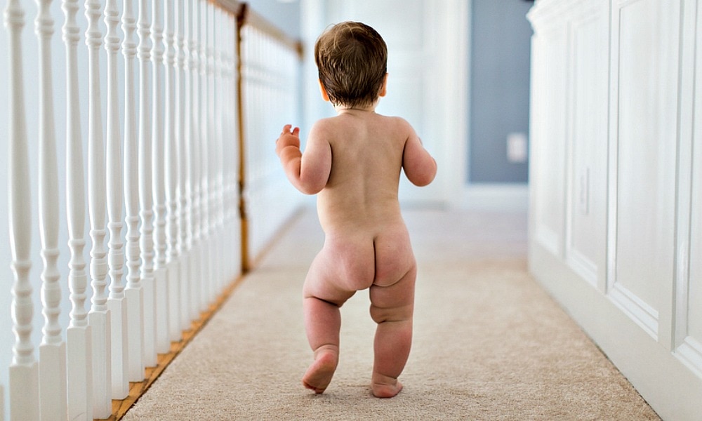 Toddler Wearing Diaper Stands Looking Out Window by Stocksy